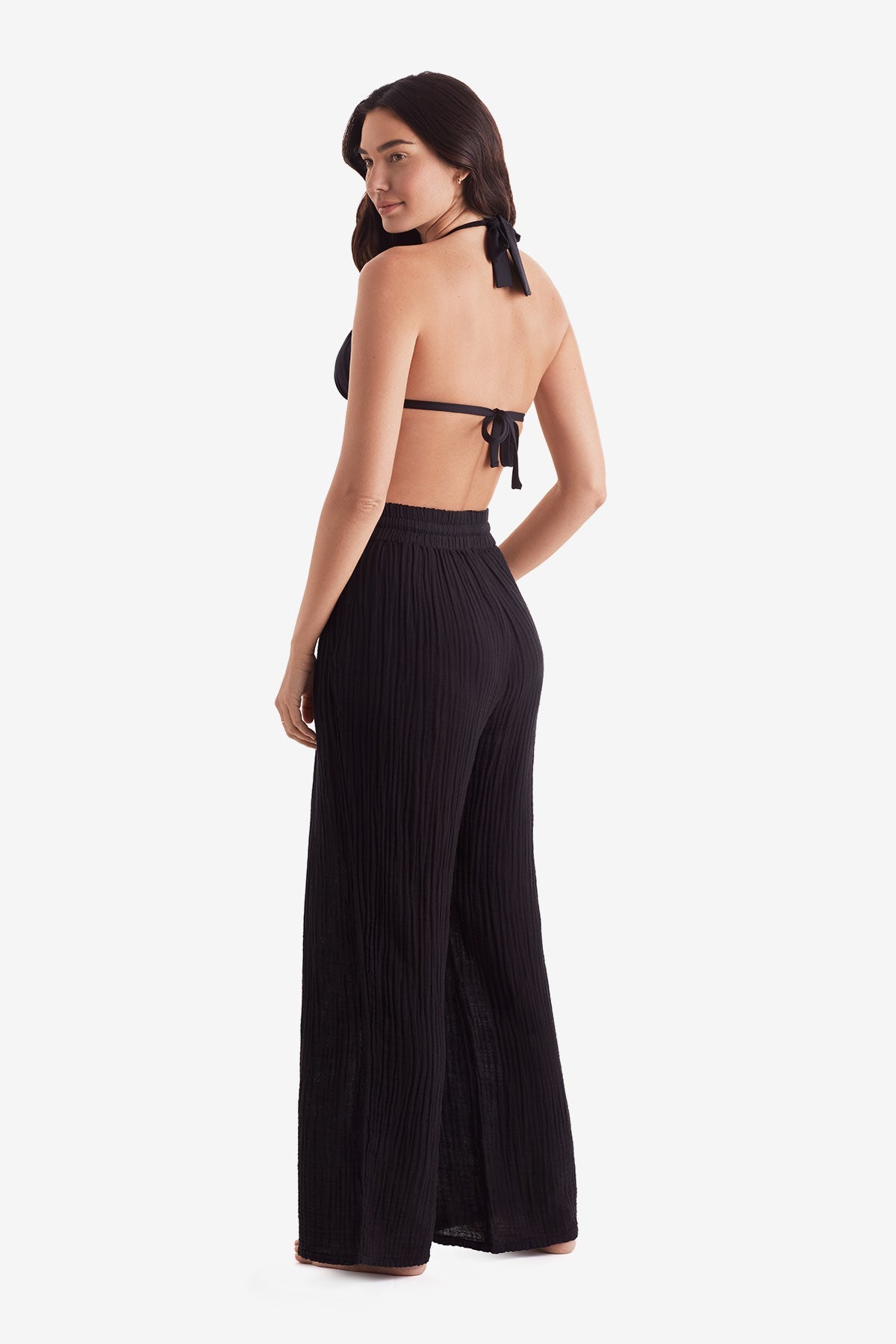 Woman turned left wearing a black bikini top and black beach pants